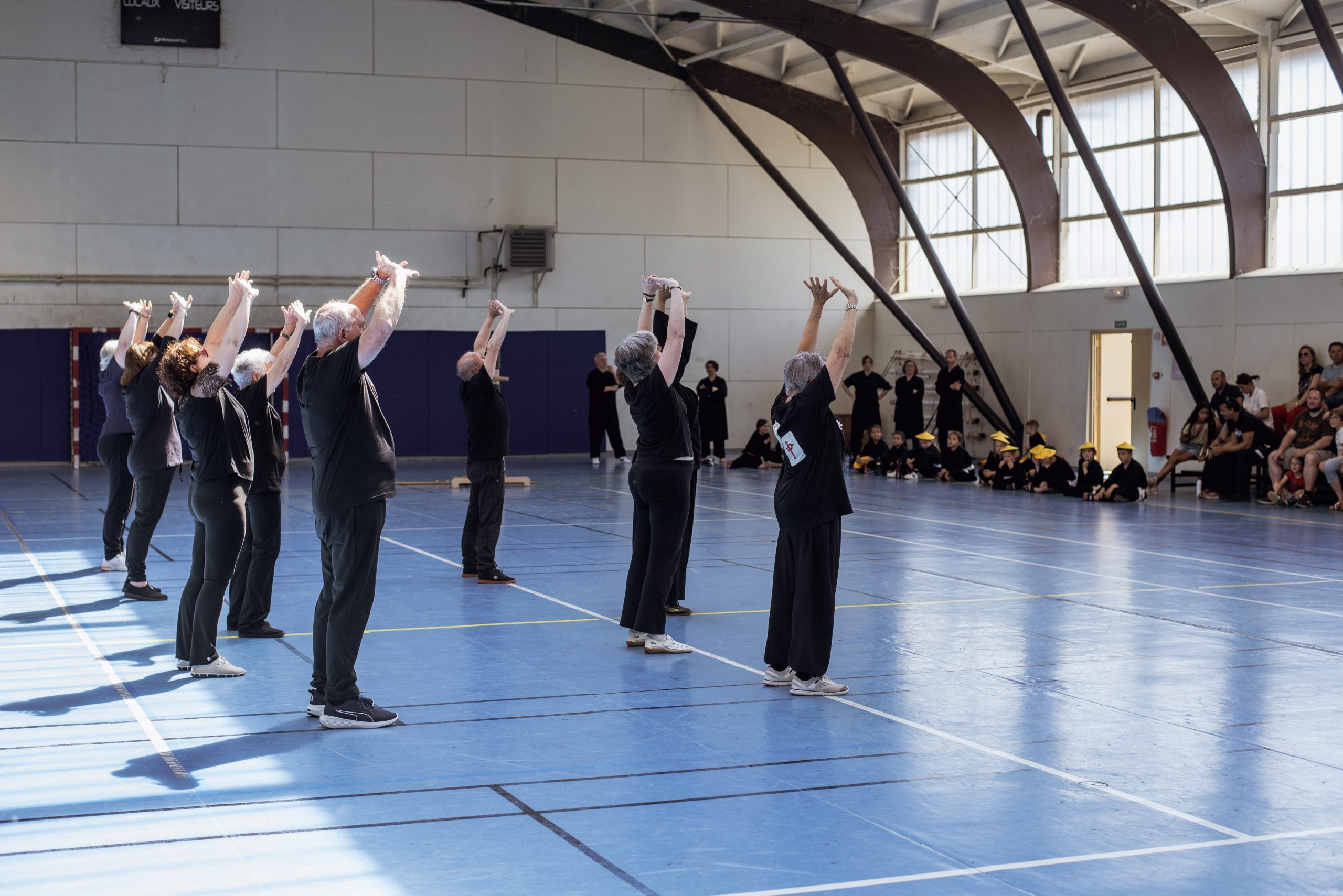 Groupe d’adhérents du club, bras levés, lors d’une démonstration de Qi Gong au gala